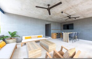 A modern living area with a sofa, wooden coffee table, chairs, a kitchen area with a bar, and ceiling fans. - Naya 6401 Tower VI in Bahia de Banderas (Punta de Mita)