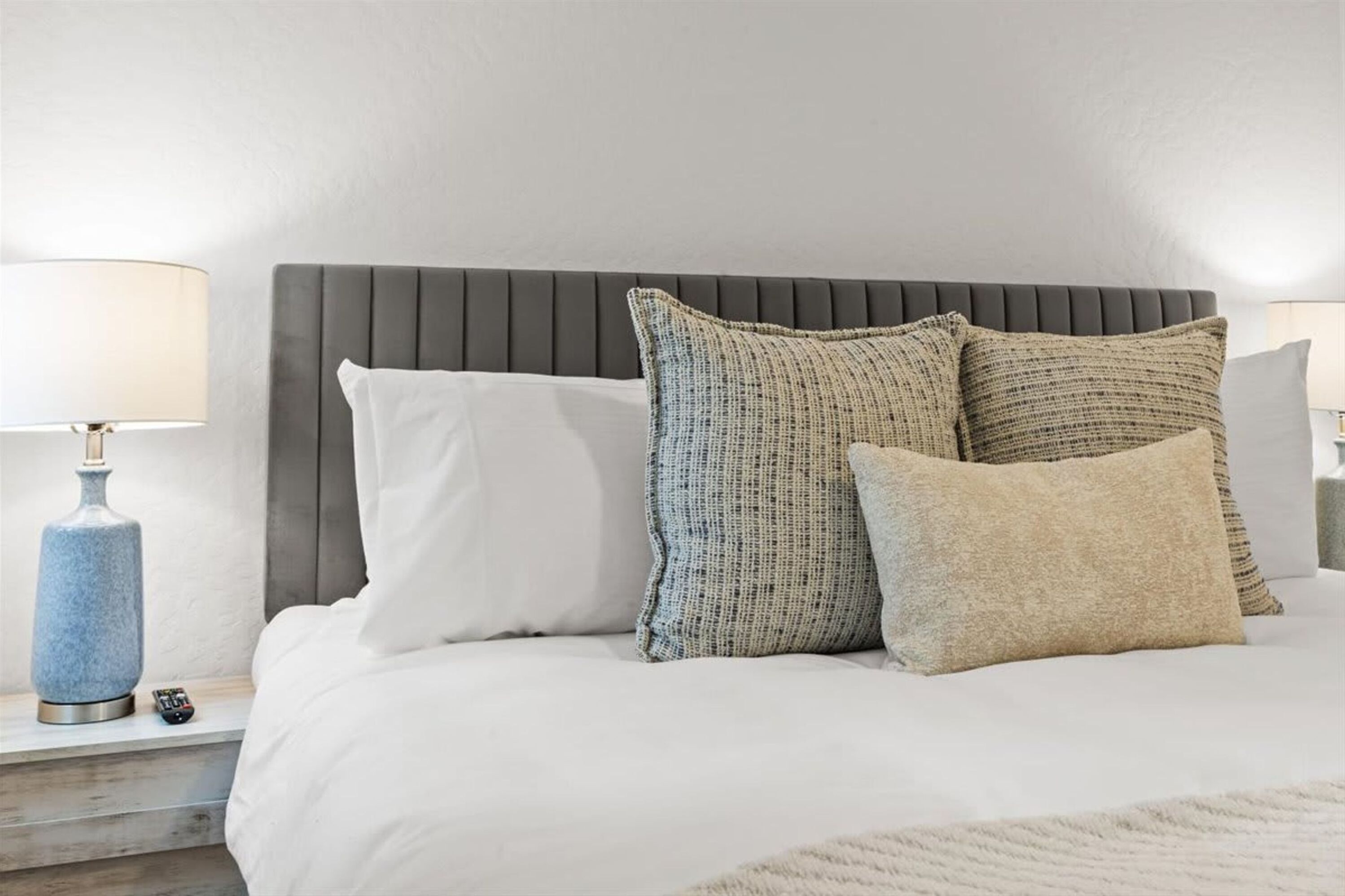A neatly made bed with a grey upholstered headboard, white bedding, and three textured pillows.