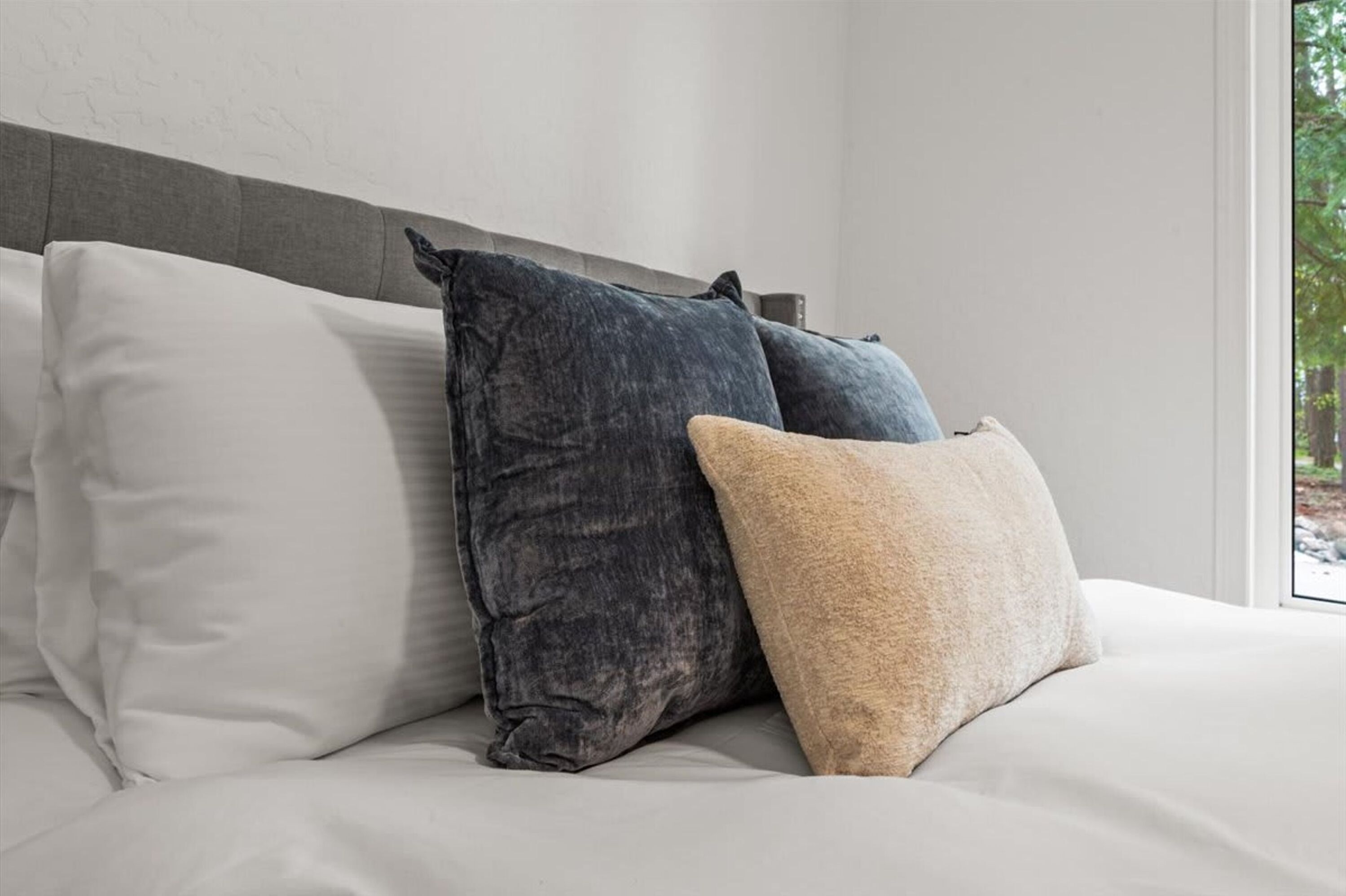 A bed with pillows, a headboard, and a window with a view.