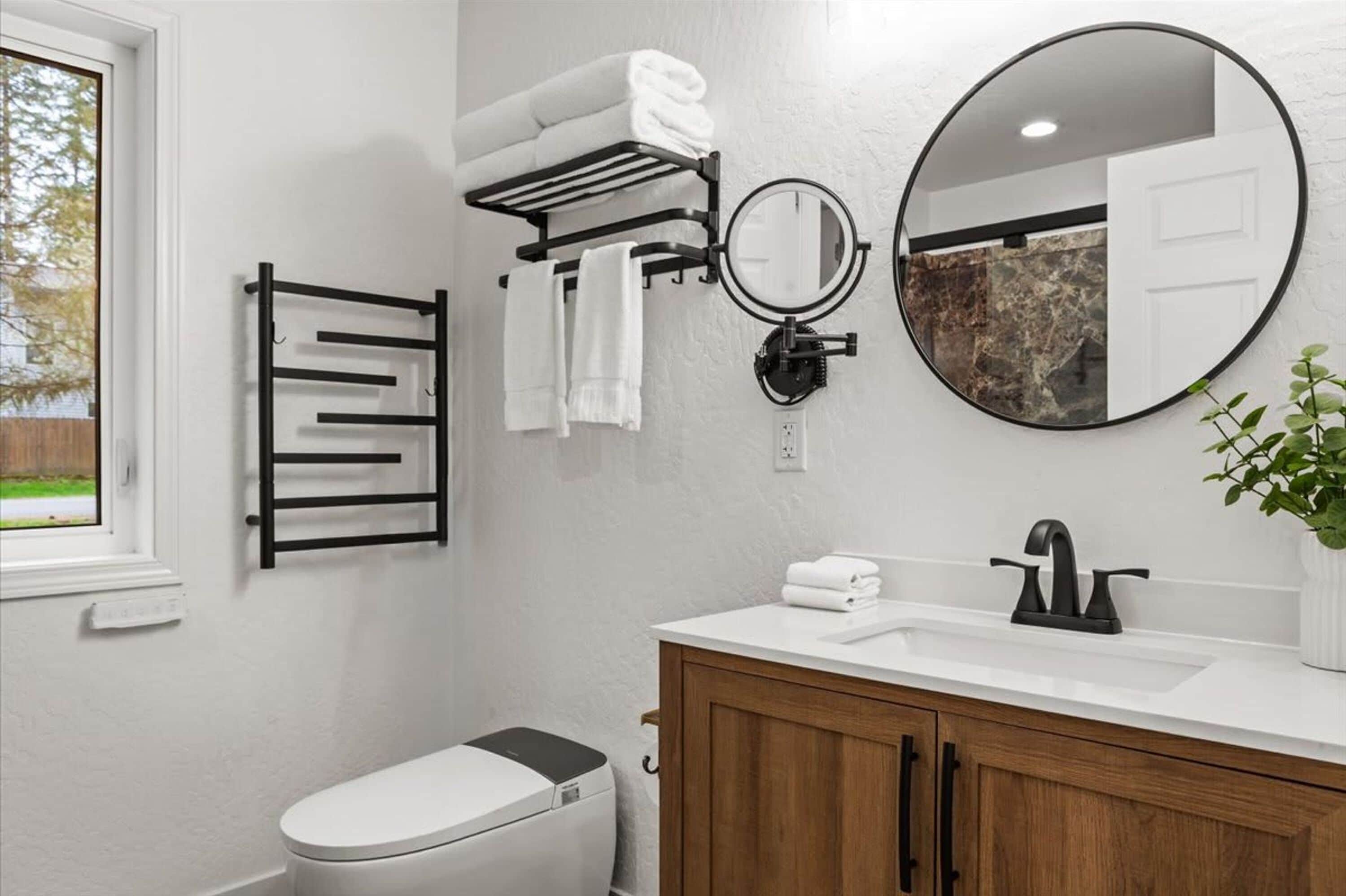 A bathroom with a toilet, a sink with a mirror, a towel rack, and a potted plant.