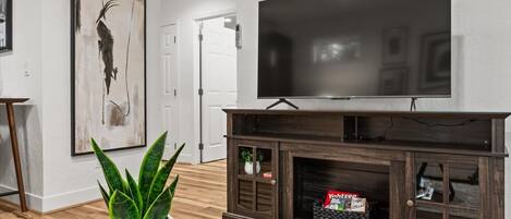 A living room with a flat-screen TV, a large abstract painting, a potted plant, and a wooden cabinet.