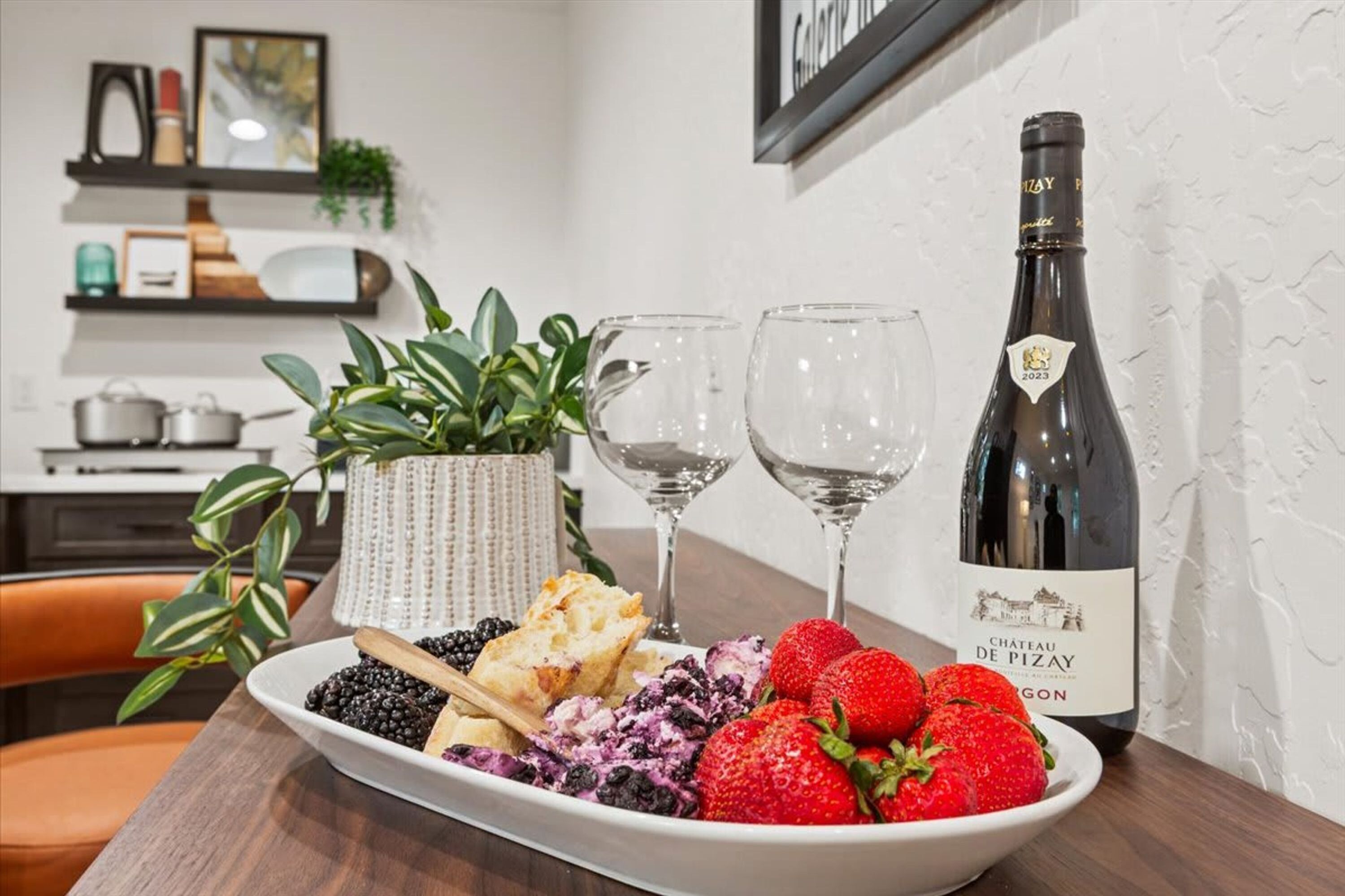A dining table with a plate of fruit, two wine glasses, and a bottle of wine.