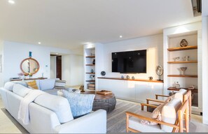 A modern living room with a sofa, armchairs, a coffee table, a TV, and built-in shelves. - 3 bed 3 5 Bath Private Pool Wide Ocean Views Condo Cualli (Punta de Mita)
