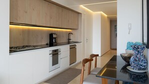 Eine moderne Küche mit Holzschränken, einem Herd und einer Kaffeemaschine. Es gibt einen Essbereich mit Tisch und Stühlen.