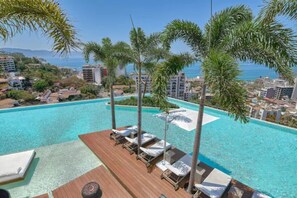 An infinity pool with lounge chairs and umbrellas, surrounded by palm trees and buildings. - 1 Bd 2bath 2nd Floor Apartment (Puerto Vallarta)