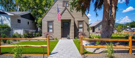 A wooden cabin with a flag, a paved walkway, and a fenced area.