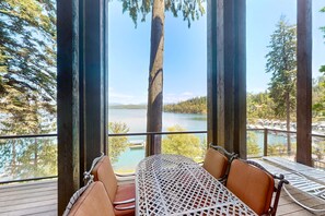 A wooden deck with a table and chairs overlooking a lake, surrounded by tall trees. - Deja View - Upper Unit (Hayden)