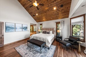 A bedroom with a wooden ceiling, a bed, a bench, a chair, and a large window. - Deja View - Upper Unit (Hayden)