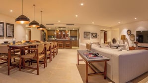 A modern living room with a sofa, dining table, chairs, pendant lights, and a kitchen in the background. - 3 Bed Condo Sleeps 12 With Pool Ocean View HK (Punta de Mita)