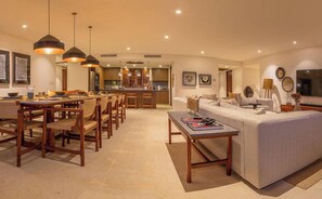 A modern living room with a sofa, dining table, chairs, pendant lights, and a kitchen in the background. - 3 Bed Condo Sleeps 12 With Pool Ocean View HK (Punta de Mita)