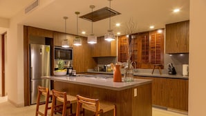 A modern kitchen with wooden cabinets, a stainless steel refrigerator, a large island with bar stools, pendant lighting, and a microwave. - 3 Bed Condo Sleeps 12 With Pool Ocean View HK (Punta de Mita)