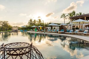 A poolside area with lounge chairs, umbrellas, and a building with a covered seating area. - Gorgeous Remodeled Hacienda de Mita Condo - HDM 905 (Punta de Mita)