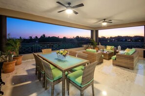 A balcony with wicker furniture, a table with a vase of flowers, and a view of the sunset. - Gorgeous Remodeled Hacienda de Mita Condo - HDM 905 (Punta de Mita)