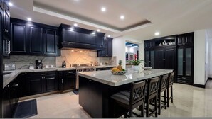 A modern kitchen with dark cabinetry, a marble countertop, and a central island with bar stools. - Gorgeous Remodeled Hacienda de Mita Condo - HDM 905 (Punta de Mita)