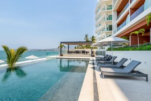 A pool area with lounge chairs, a covered seating area, and a view of the ocean. - Luxury 2 bed 2 Bath Beach Front Condo - Bucerias - Casa Del Mar 105 (Bucerías)