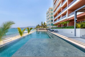 A pool with a view of the sea, a covered seating area, and a multi-story building with balconies. - Luxury 2 bed 2 Bath Beach Front Condo - Bucerias - Casa Del Mar 105 (Bucerías)