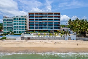 Ein Hotel direkt am Strand mit mehreren Etagen, einem Pool und Palmen.