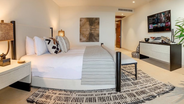 A modern bedroom with a bed, bedside tables, a desk, a television, and a ceiling fan. - 3 bed Condo With Pool Ocean View (Punta de Mita)
