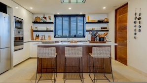 A modern kitchen with a large window, a built-in oven, and a bar area with stools. - 3 bed Condo With Pool Ocean View (Punta de Mita)