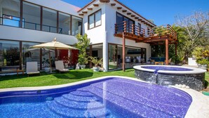 Una casa moderna de dos pisos con piscina, patio cubierto y jardín.