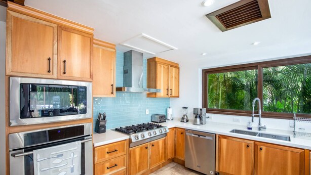 Una cocina moderna con armarios de madera, electrodomésticos de acero inoxidable, un ventanal con vistas a zonas verdes y un horno empotrado.