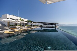 Ein Pool ohne Ende mit klarem Wasser, Liegestühlen, Sonnenschirmen und Blick auf das Meer.
