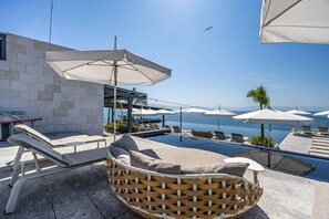 Ein Poolbereich mit Liegestühlen, Sonnenschirmen und Blick auf den Ozean.