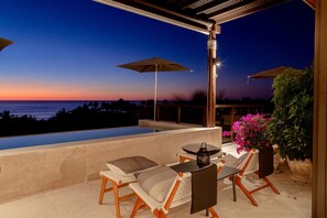 A terrace with a view of the ocean at dusk, featuring a pool, lounge chairs, and umbrellas. - Lux 3 Bed Condo With Ocean View Pool Houskeeping (Punta de Mita)