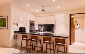A modern kitchen with a black countertop, stainless steel appliances, and wooden bar stools. - Lux 3 Bed Condo With Ocean View Pool Houskeeping (Punta de Mita)
