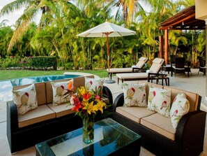 A poolside area with a sofa set, lounge chairs, and a table with a vase of flowers. - Casa Sabba at Las Palmas Punta Mita Bunk Room (Punta de Mita)