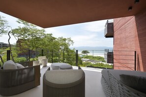 Een balkon met zitplaatsen buiten, uitzicht op de zee en een rood gebouw.