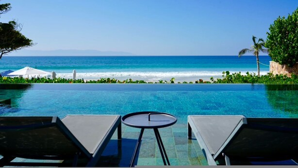 Ein Infinity-Pool mit Meerblick, Liegestühle und ein kleiner Tisch.