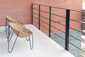 Ein Balkon mit zwei Korbstühlen, einem Metallgeländer und Blick auf ein Gebäude.
