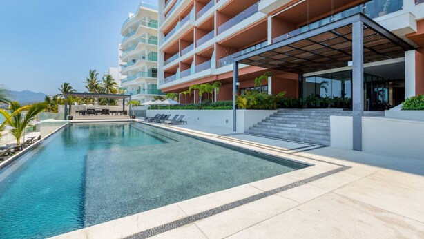 A modern hotel with a swimming pool, outdoor seating, and a multi-story building. - Luxury 2 Bed 2 Bath Beachfront Condo - Bucerias (Bucerías)