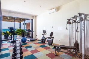 Ein Fitnessraum mit Trainingsgeräten, einer Bank und Blick auf den Ozean.
