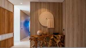 A modern interior with wooden panel walls, a round woven wall hanging, and a wooden console table with vases. - Naya 3302 Tower III in Punta de Mita (Punta de Mita)