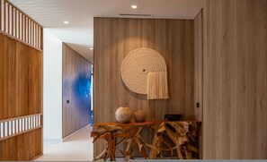 Ein modernes Interieur mit Holzpaneelen, einem runden gewebten Wandbehang und einem Holztischchen mit Vasen.