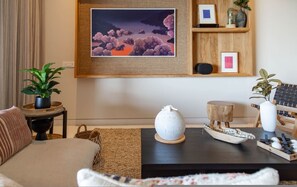 Ein Wohnzimmer mit einer Couch, einem Couchtisch mit Dekoration, einem gerahmten Bild an der Wand und einer Topfpflanze.