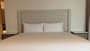 Un letto grande con una testiera imbottita, due cuscini e una coperta bianca liscia.
