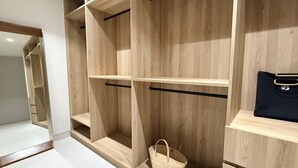 Un armadio in legno con ripiani multipli e un'asta appendiabiti, un cesto di vimini e una borsa nera.