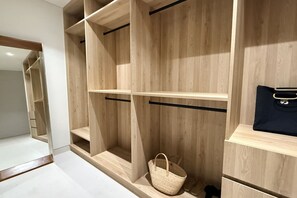 Ein Holzschrank mit mehreren Einlegeböden und Kleiderstange, ein gewebter Korb und eine schwarze Handtasche.