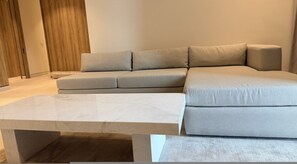 Ein modernes Wohnzimmer mit einer Eckcouch, einem Marmortisch und Holzboden.