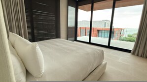 Una camera da letto moderna con un letto grande, vista su un edificio attraverso finestre a tutta parete e un balcone.