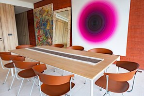 Ein Konferenzraum mit einem langen Tisch, orangefarbenen Stühlen, einem farbenfrohen abstrakten Gemälde und einem großen Spiegel.