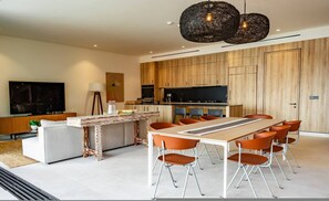 Eine moderne Küche mit Holzausstattung, ein Essbereich mit orangefarbenen Stühlen und ein großer Fernseher an der Wand.
