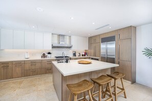 A modern kitchen with wooden cabinets, a large island with stools, stainless steel appliances, and a white countertop. - Casa Bahia in Punta Mita (Punta de Mita)