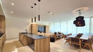 A modern kitchen with a central island, a dining area with a large table and chairs, and a living room with a sofa and TV. - Naya 4101 Tower IV in Punta De Mita (Punta de Mita)