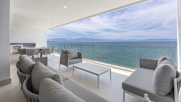 Un balcon moderne offrant une vue sur la mer, avec un espace repas et un coin salon.