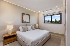 A modern bedroom with a large bed, bedside tables, a wall-mounted artwork, and a window with a view. - 4-bed Beachfront Lux Apartment (Bucerías)