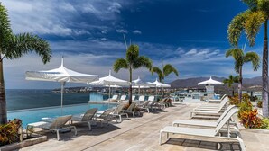 Un espace aménagé au bord de la piscine, avec des chaises longues et des parasols, offrant une vue sur un plan d’eau et des montagnes.